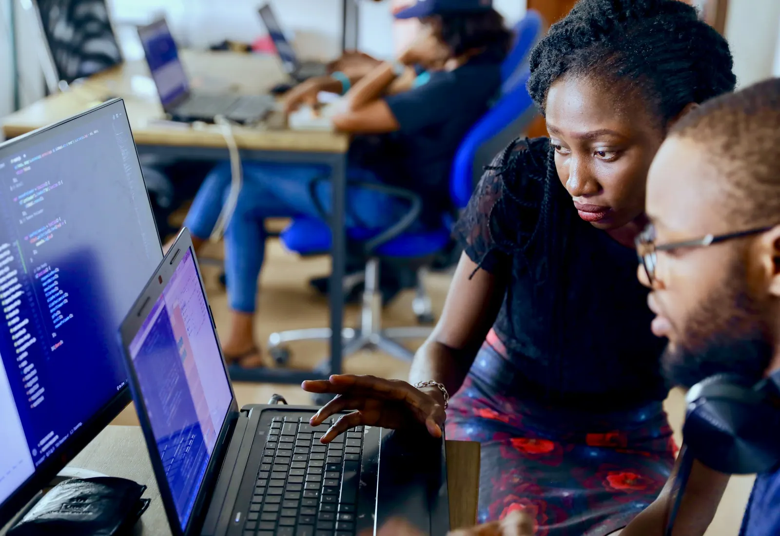 Two developers reviewing code together on a laptop in a shared workspace